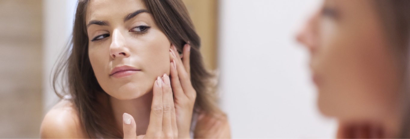 Woman checking her face in the mirror for acne scarring
